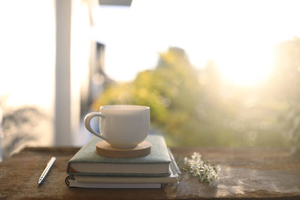 自然光が差し込む木のテーブルの上の白いコーヒーカップとノート - meeting food nature foods and drinks ストックフォトと画像