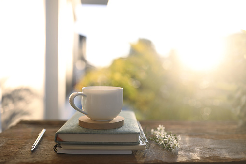 white coffee cup and notebook on wooden table with natural sunlight