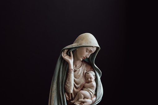 Statue of the virgin Mary holding the baby Jesus against a black background with copy space