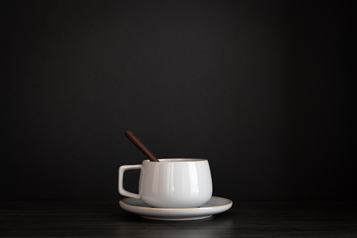Small grey coffee cup on a saucer with a small dark wood spoon in it on a black background shot from table top with copy space