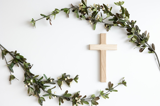 Simple wood Christian cross and curved branches with green leaves and white berries on a white background with copy space