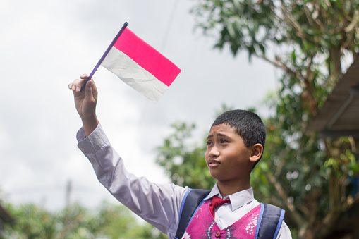 indonesian school student holding flag during independence day. proud primary pupil with indonesia flag outdoor