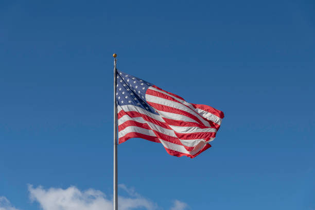 A Large American Flag Blows in the Wind A large American flag blows in the wind against a bright blue sky. flagpole stock pictures, royalty-free photos & images