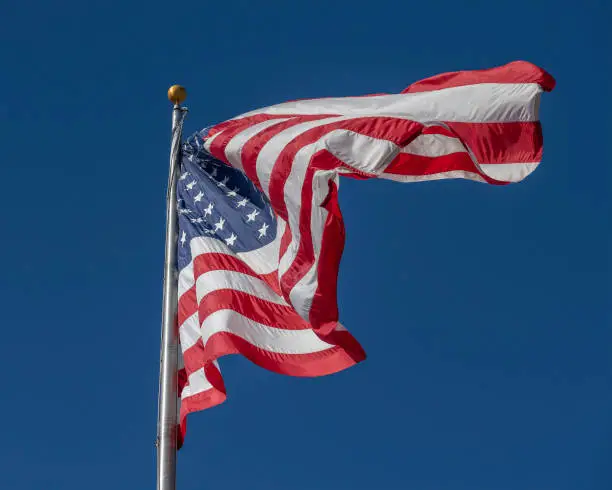 A large American flag blows in the wind against a bright blue sky.