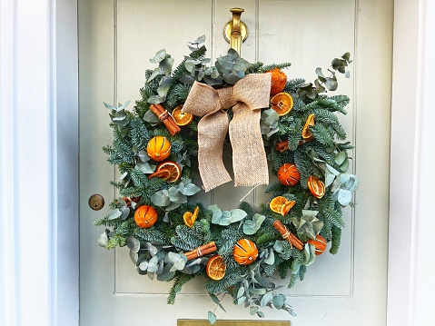 A beautiful Christmas wreath decorated with dried orange slices and cinnamon sticks hangs on a white wooden front door.