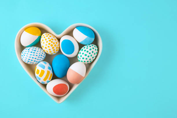 Colorful dyed easter eggs in heart shaped bowl on blue background