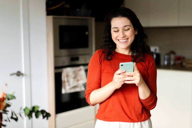 istock Young happy woman using her phone in the kitchen 1447447869