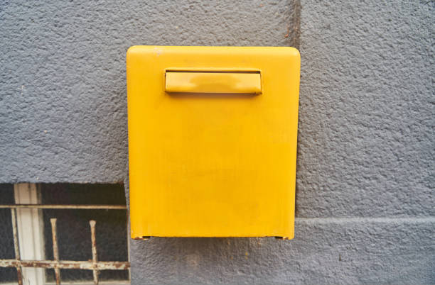 istock Yellow mailbox on the gray wall of a building with a window 1447452036