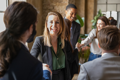 Smiling mature adult businesswoman shaking hands with a coworker during a meeting with colleagues, confident and happy business people greeting and congratulate on the successes