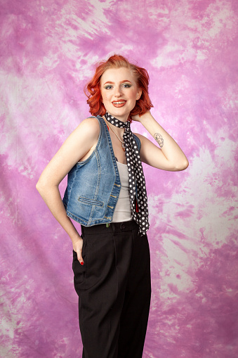 Studio portrait of a young red-haired white woman dressed in retro style on a pink background