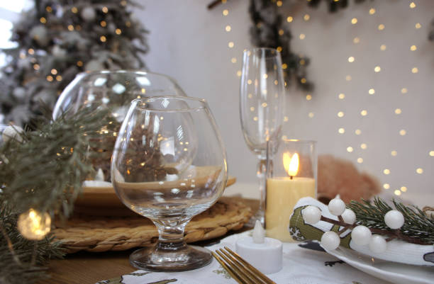 istock Christmas and New Year table setting with decorations. Festive dinner atmosphere. Wine glasses, fir branches, candles, a plate with a napkin. Christmas garlands in the background. 1447461811