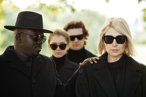 Minimal portrait of woman wearing all black at outdoor funeral ceremony with friend comforting her