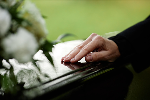 Closeup of womans hand on coffin saying goodbye at outdoor funeral ceremony, copy space