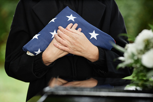 Close up of woman holding American flag at outdoor funeral ceremony for veteran, copy space