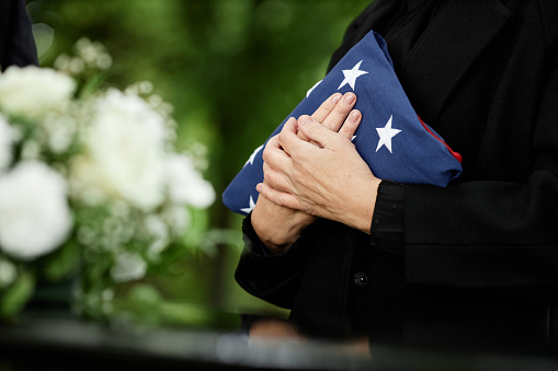 Woman holding American flag to chest at outdoor funeral ceremony for veteran, closeup