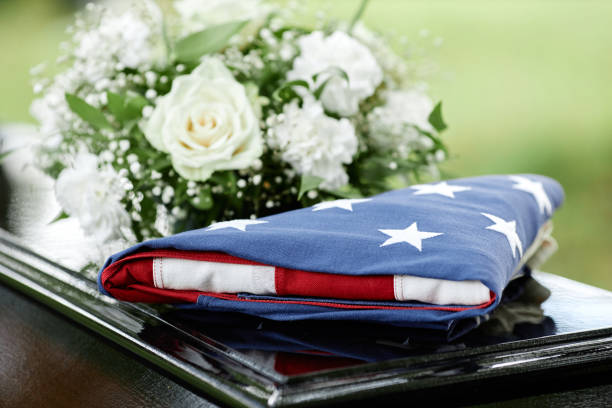 Closeup of folded American flag on coffin with flowers at outdoor funeral ceremony, copy space