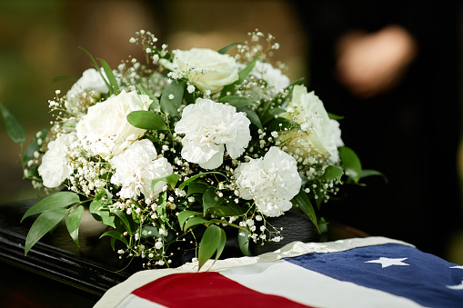 Closeup of American flag on coffin with flowers at outdoor funeral ceremony for army veteran, copy space
