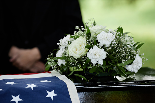 Closeup of coffin with flowers at outdoor funeral ceremony for army veteran, copy space