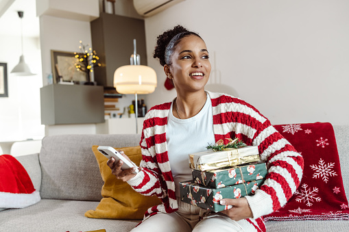 Young woman preparing gifts for Xmas and uses a smart phone phone