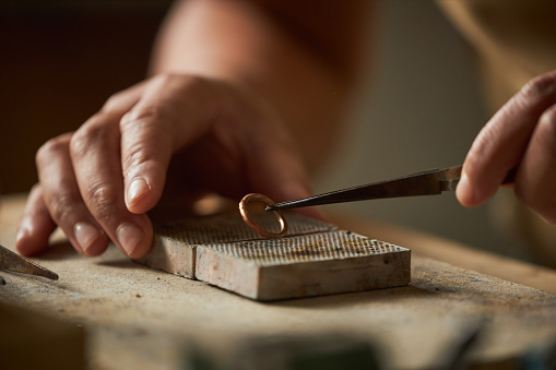 Close up of artisan jeweler holding handmade ring with tweezers in cozy rustic setting, copy space