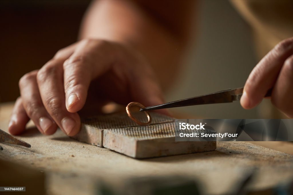 Close up of artisan jeweler holding handmade ring Close up of artisan jeweler holding handmade ring with tweezers in cozy rustic setting, copy space Jewelry Stock Photo