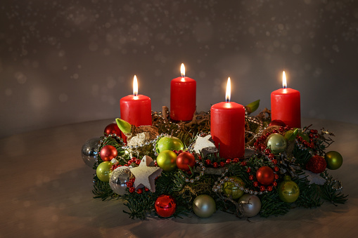 Three small white christmas star shaped candles burn on red mantle. Blurred pine cones lay in the dark background. The flames are a brilliant white. This picture has a romantic Christmas season feeling.