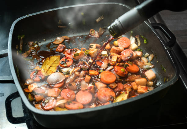 red wine is poured into a cooking pan of steaming roasted vegetables to deglaze for a sauce base from carrots, onions, leeks, celery and bay leaves, copy space, selected focus - bay leaf healthy eating food and drink red imagens e fotografias de stock