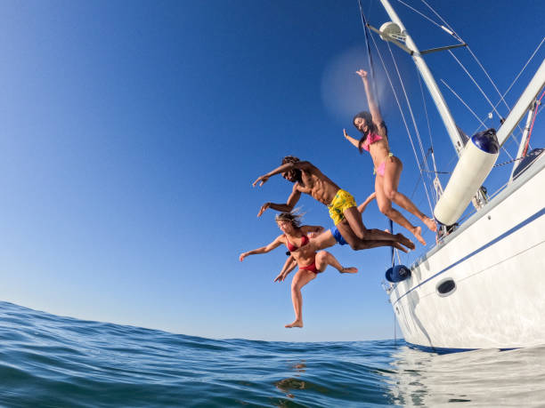 groupe d’amis plongeant dans l’eau lors d’une excursion en voilier, jeunes sautant dans l’océan en vacances d’été à partir d’une voile, s’amusant, style de vie de vacances de luxe - swimwear caribbean sea beach water photos et images de collection