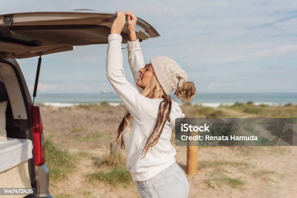 A Woman With White Winter Bobble Hat Opening Or Closing The Trunk Door Of Her Parked Camper Van Close To The Beach Van Life Concept Stock Photo - Download Image Now