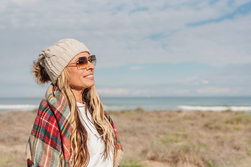 portrait of a woman in knitted winter bobble hat enjoying a sunny winter or autumn day at the beach