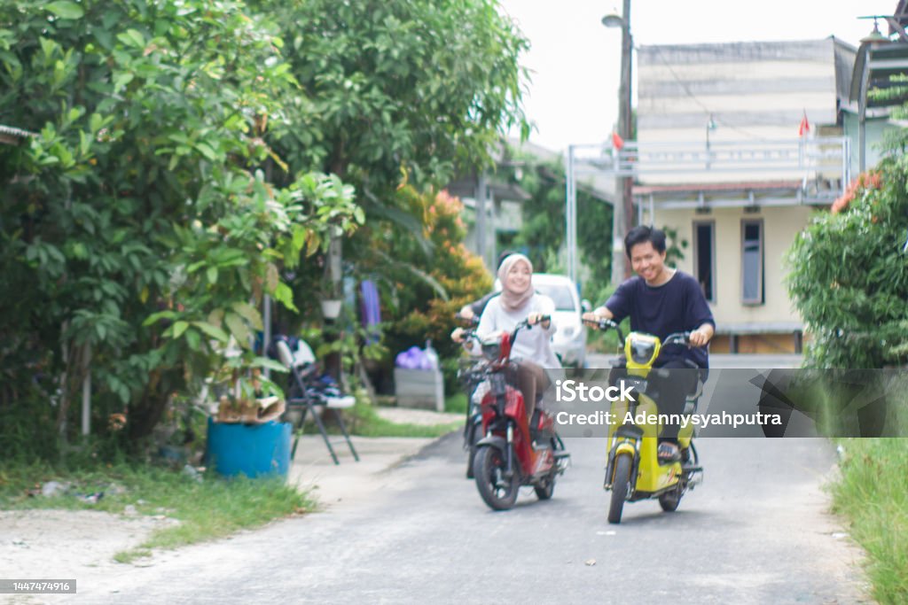 young couple riding electric bikes in residential area 20-24 Years Stock Photo