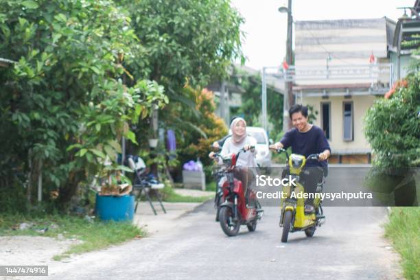 Young Couple Riding Electric Bikes In Residential Area Stock Photo - Download Image Now