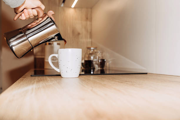 istock A woman's hand pours black coffee from a geyser coffee maker into a white mug, kitchen interior. Selective focus 1447475706