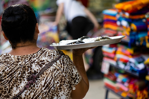 In Playa del Carmen, Mexico the back of a local woman is seen as she walks along Avenida Quinta with a platter of homemade food for sale.