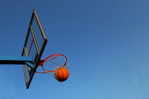 A basketball in a basket on an outdoor basketball court. Basketball match, ring and basket basketball on the sky background. Ball and basket against the sky in the goal.