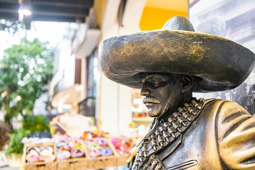 In Playa del Carmen, Mexico a bronze statue of an old fashioned bandit dressed man in a sombrero and wearing a bandolier full of ammunition sits outside a retail shop on tourist destination, Avenida Quinto, 5th Avenue.