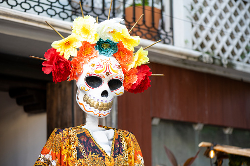In Playa del Carmen, Mexico just after Day of the Dead a large skeloton statue with a sugar skull face and traditional clothing remains on display along 5th Avenue wearing a crown of flowers.