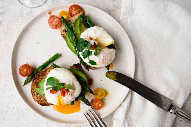 pochierte eier auf toast mit avocado, spargel, tomaten und spross für gesundes frühstück - poached stock-fotos und bilder