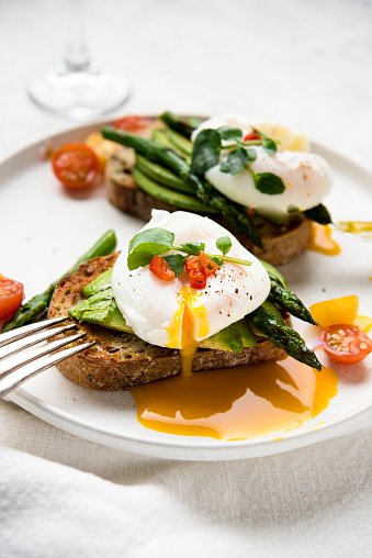 Poached eggs on toast with avocado, asparagus, tomatoes and sprout for healthy breakfast.