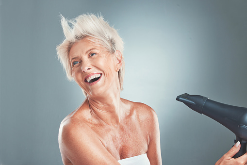 Hair, hairdryer and senior woman in studio for beauty, stylish and hair care on grey background mockup. Grey hair, mature woman and elderly woman wellness model dry hair, happy, relax and having fun