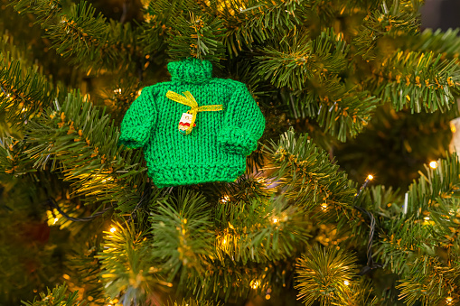 Small knitted green sweater and garlands, craft decor on branches of Christmas tree. Christmas and new year concept