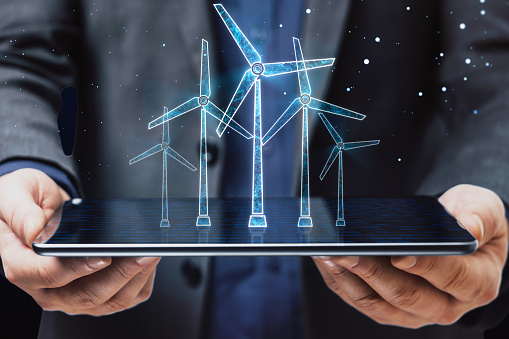 Close up of businessman hand holding tablet with glowing digital wind mill turbine hologram on blue background. Wind generator concept