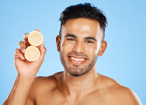 Health, lemon and skincare for man with citrus fruit for facial, vitamin c and wellness with a smile on blue background. Dermatology, beauty and healthy food portrait for clean, glow and skin healthy