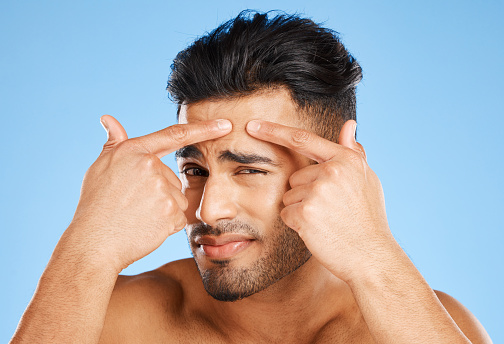 Skincare, confused and portrait of man with hands on face feeling wrinkle line with anxiety, doubt and stress. Model in studio touching skin with facial aesthetic problem on blue background.