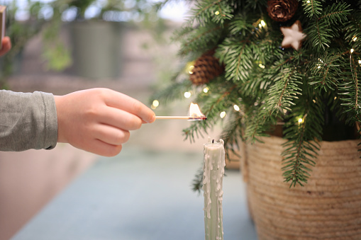 Child hand holds match above candle light festive background christmas tree soft focus christmas decorations