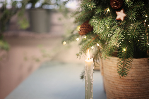 Burning candle in front of decorated christmas tree festive background soft focus copy space