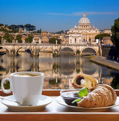 Saint Peter's Basilica and Tiber river against cup of fresh coffee with croissant in Rome, Italy