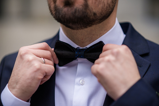 the hands of the groom bow tie. stylish groomsmen helping happy groom getting ready in the morning for wedding ceremony. luxury man in suit in room. wedding day. close up