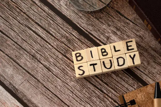 Bible study text written on wooden cubes, holy Bible book, notebook, pen, and magnifying glass on wooden background. Copy space. Top table view.
