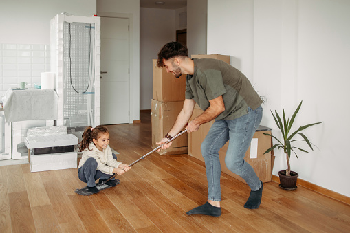 Father and daughter having fun in new apartment while cleaning the floors